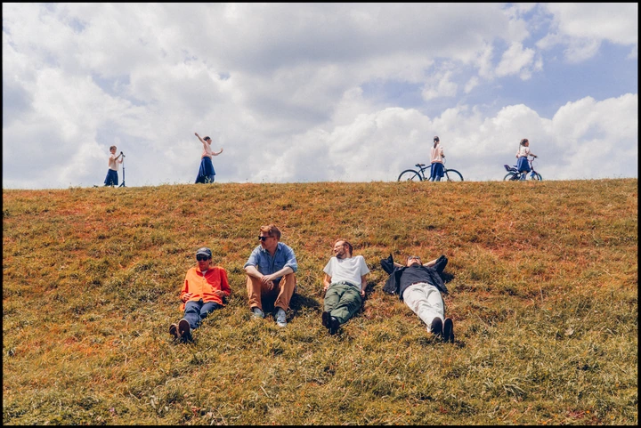 Django Django seated in an open field beneath a wide sky